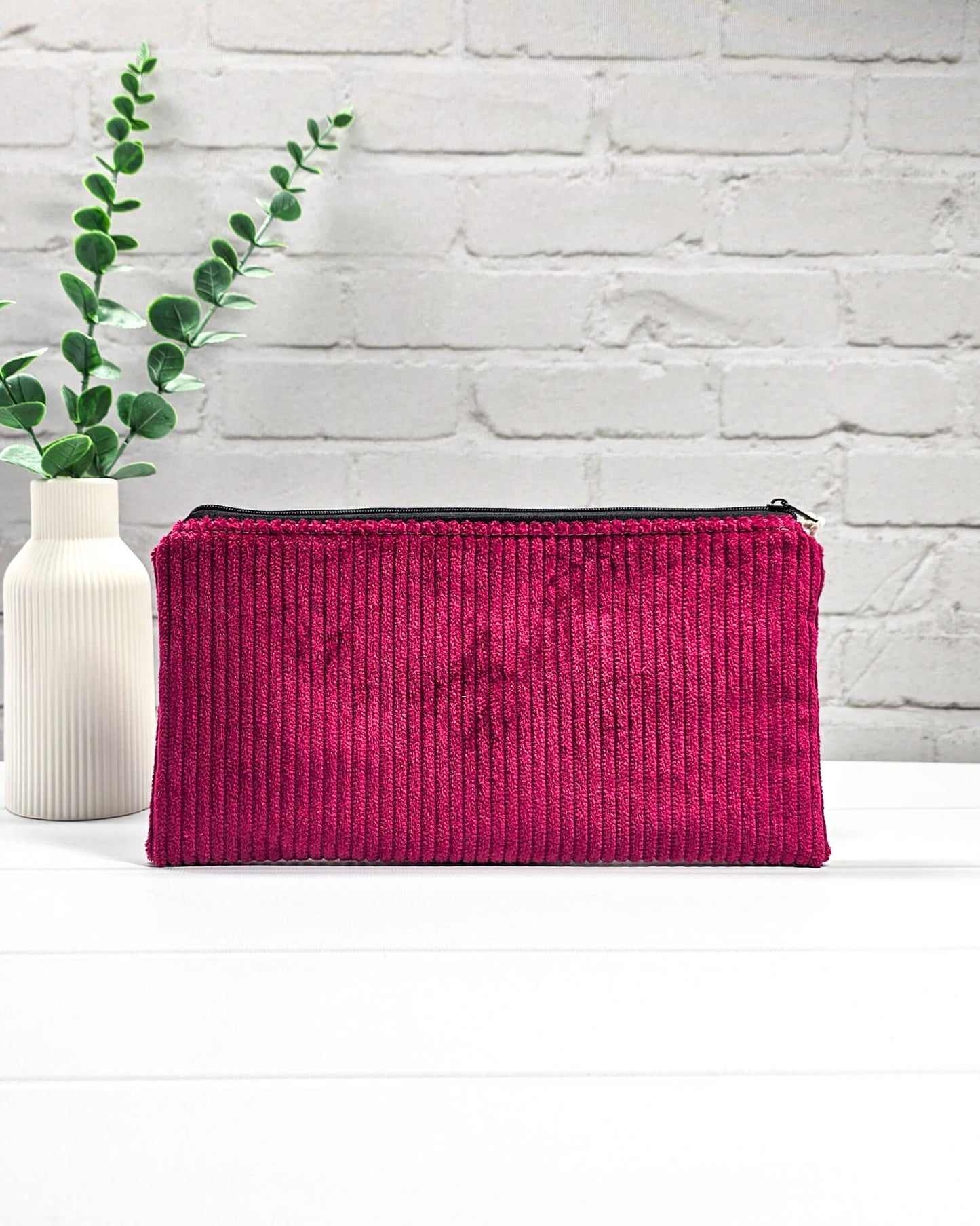 Kleine magentafarbene Reißverschlusstasche aus Cord-Stoff für Strickzubehör, liegend auf weißem Untergrund mit einer Schere, Garnsträngen und Holznadeln. Handgenäht in Bayern von Nadelmikado.