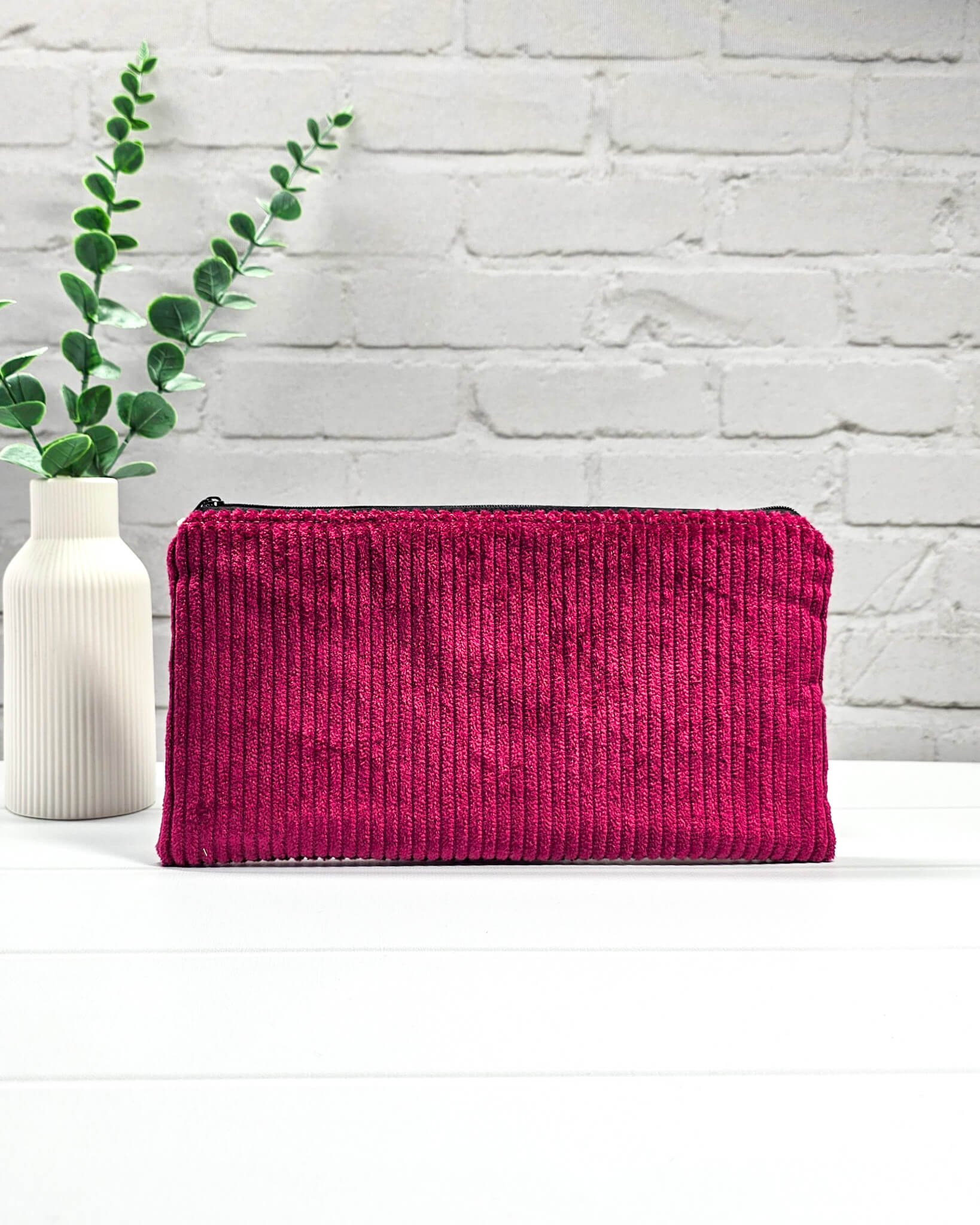 Kleine magentafarbene Reißverschlusstasche aus Cord-Stoff für Strickzubehör, liegend auf weißem Untergrund mit einer Schere, Garnsträngen und Holznadeln. Handgenäht in Bayern von Nadelmikado.
