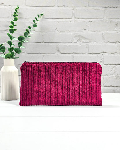 Kleine magentafarbene Reißverschlusstasche aus Cord-Stoff für Strickzubehör, liegend auf weißem Untergrund mit einer Schere, Garnsträngen und Holznadeln. Handgenäht in Bayern von Nadelmikado.