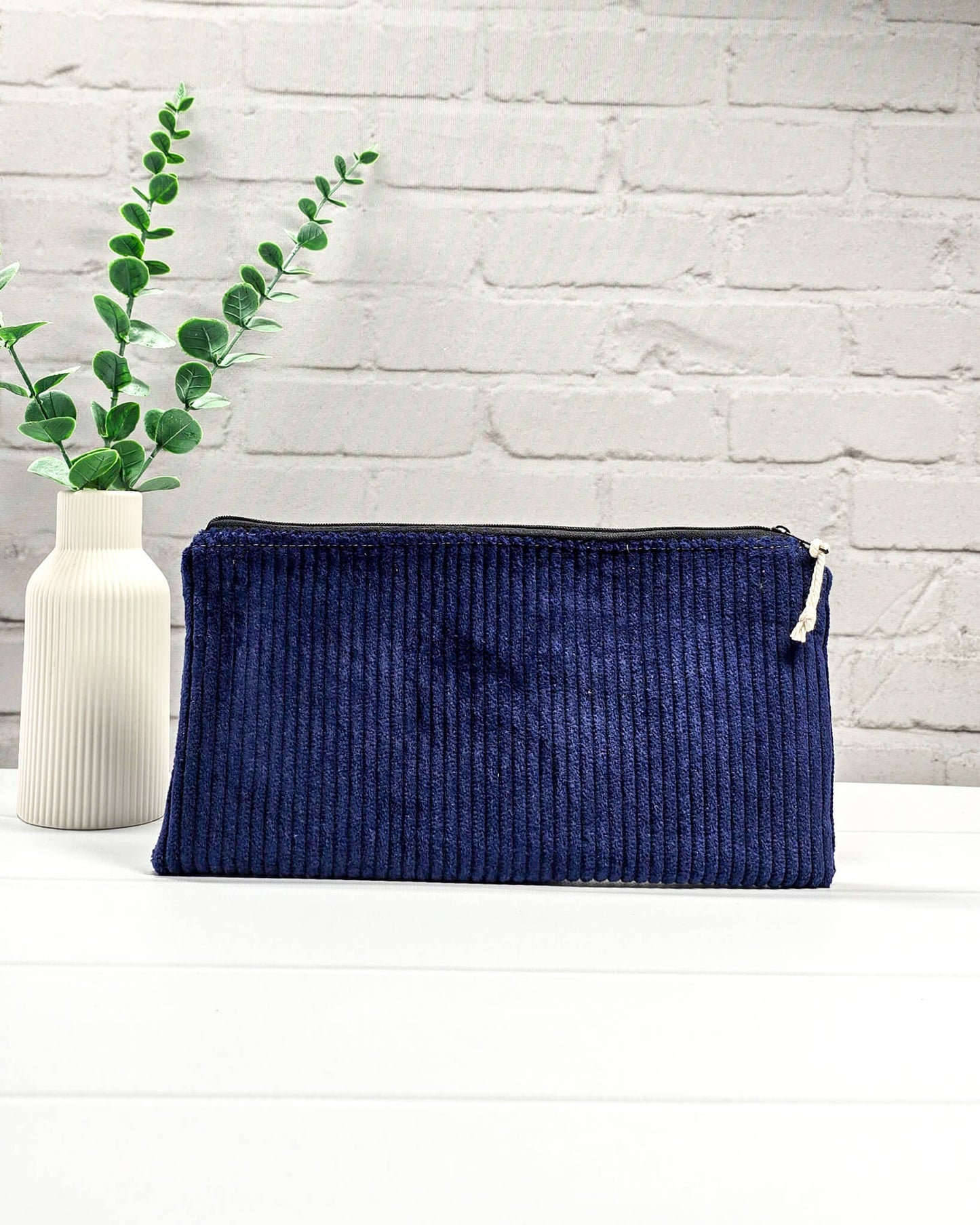 Kleine navyblaue Reißverschlusstasche aus Cord-Stoff für Strickzubehör, liegend auf weißem Untergrund mit einer Schere, Garnsträngen und Holznadeln. Handgenäht in Bayern von Nadelmikado.
