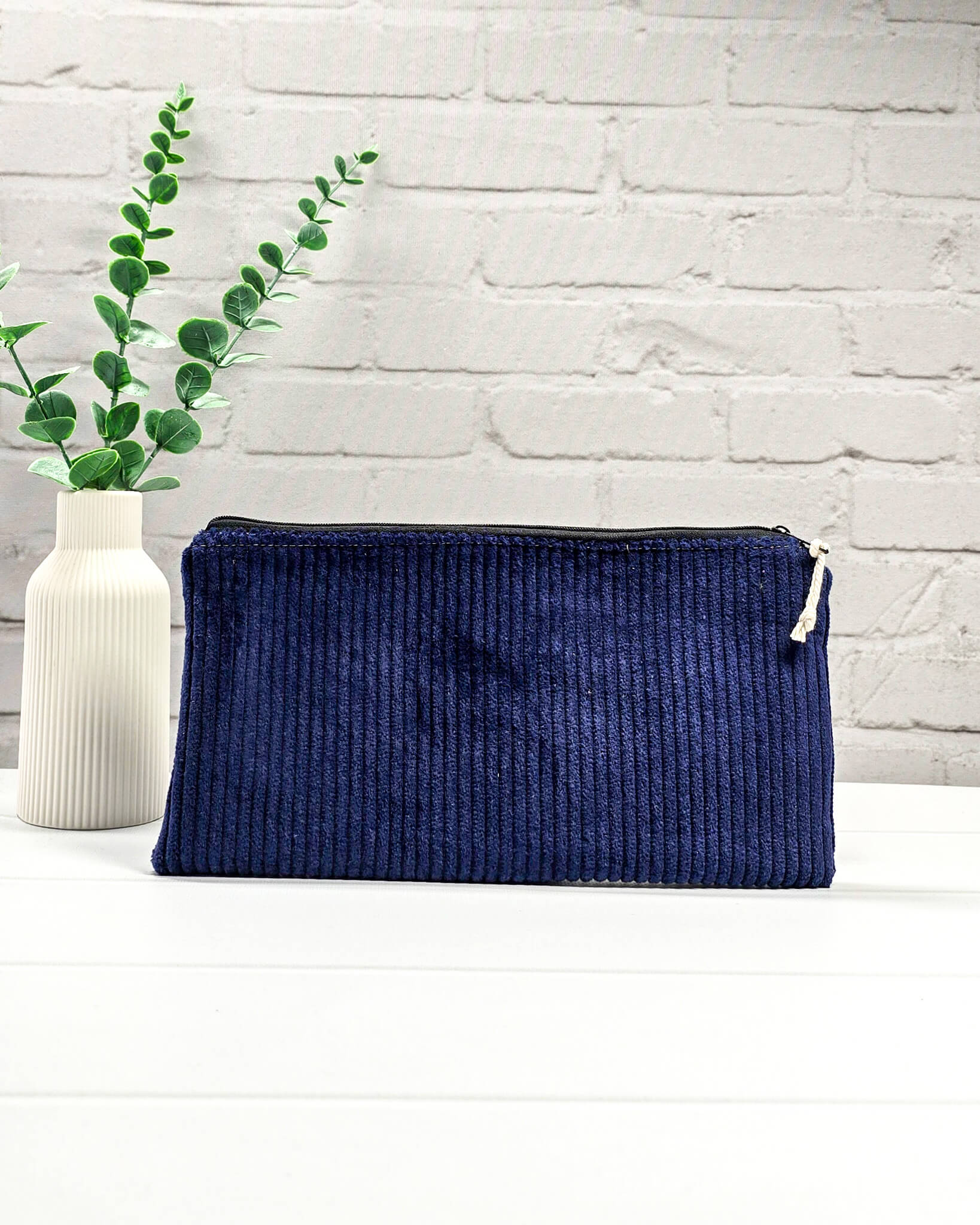 Kleine navyblaue Reißverschlusstasche aus Cord-Stoff für Strickzubehör, liegend auf weißem Untergrund mit einer Schere, Garnsträngen und Holznadeln. Handgenäht in Bayern von Nadelmikado.