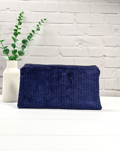 Kleine navyblaue Reißverschlusstasche aus Cord-Stoff für Strickzubehör, liegend auf weißem Untergrund mit einer Schere, Garnsträngen und Holznadeln. Handgenäht in Bayern von Nadelmikado.