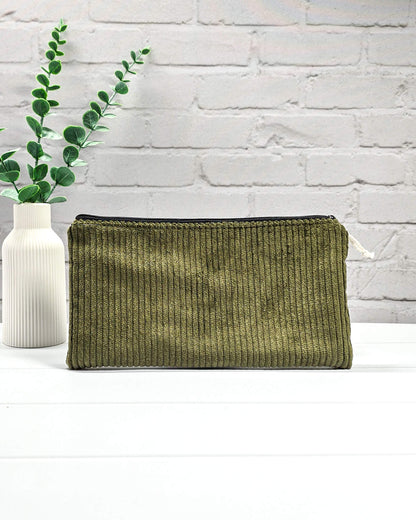 Kleine olivgrüne Reißverschlusstasche aus Cord-Stoff für Strickzubehör, liegend auf weißem Untergrund mit einer Schere, Garnsträngen und Holznadeln. Handgenäht in Bayern von Nadelmikado.