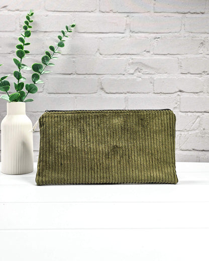 Kleine olivgrüne Reißverschlusstasche aus Cord-Stoff für Strickzubehör, liegend auf weißem Untergrund mit einer Schere, Garnsträngen und Holznadeln. Handgenäht in Bayern von Nadelmikado.