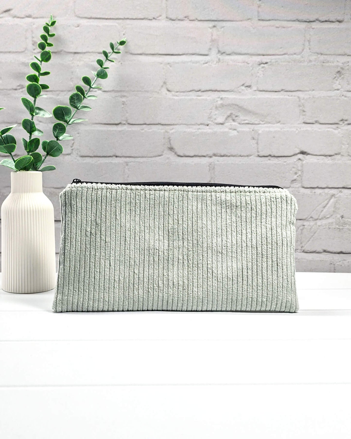 Kleine Reißverschlusstasche aus hellgrünem Cord-Stoff für Strickzubehör, flach liegend auf weißem Untergrund mit Schere, Garn und Nadeln. Handgenäht in Bayern von Nadelmikado.