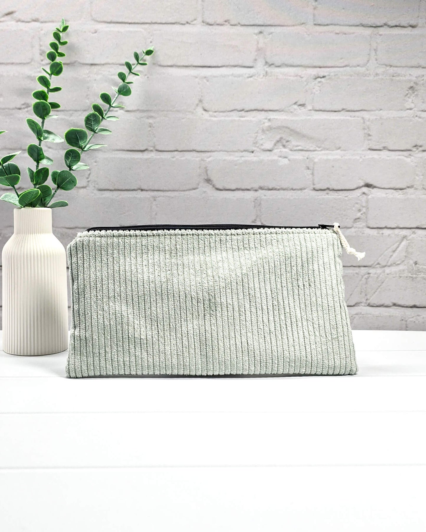 Kleine Reißverschlusstasche aus hellgrünem Cord-Stoff für Strickzubehör, flach liegend auf weißem Untergrund mit Schere, Garn und Nadeln. Handgenäht in Bayern von Nadelmikado.