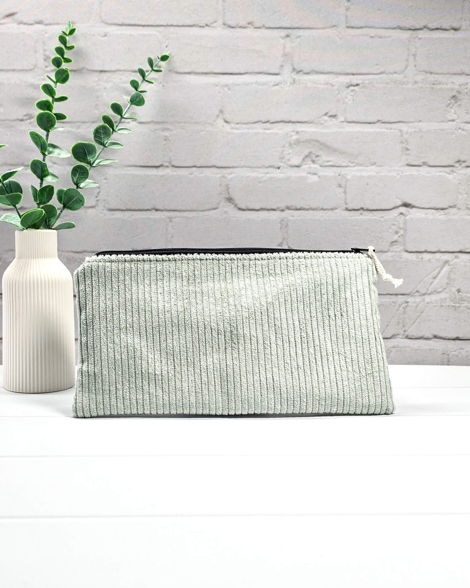 Kleine Reißverschlusstasche aus hellgrünem Cord-Stoff für Strickzubehör, flach liegend auf weißem Untergrund mit Schere, Garn und Nadeln. Handgenäht in Bayern von Nadelmikado.