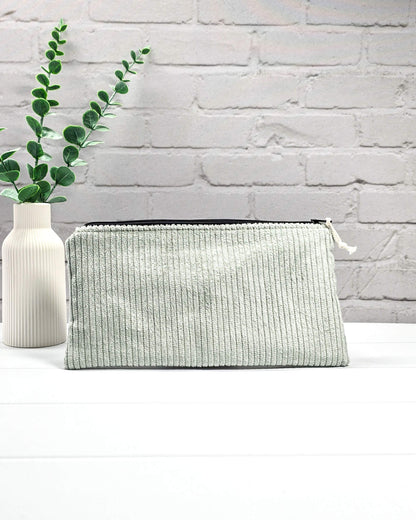 Kleine Reißverschlusstasche aus hellgrünem Cord-Stoff für Strickzubehör, flach liegend auf weißem Untergrund mit Schere, Garn und Nadeln. Handgenäht in Bayern von Nadelmikado.