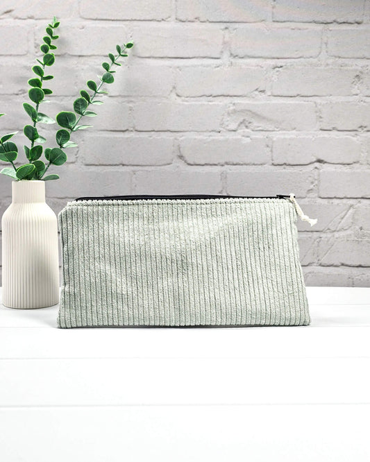 Kleine Reißverschlusstasche aus hellgrünem Cord-Stoff für Strickzubehör, flach liegend auf weißem Untergrund mit Schere, Garn und Nadeln. Handgenäht in Bayern von Nadelmikado.