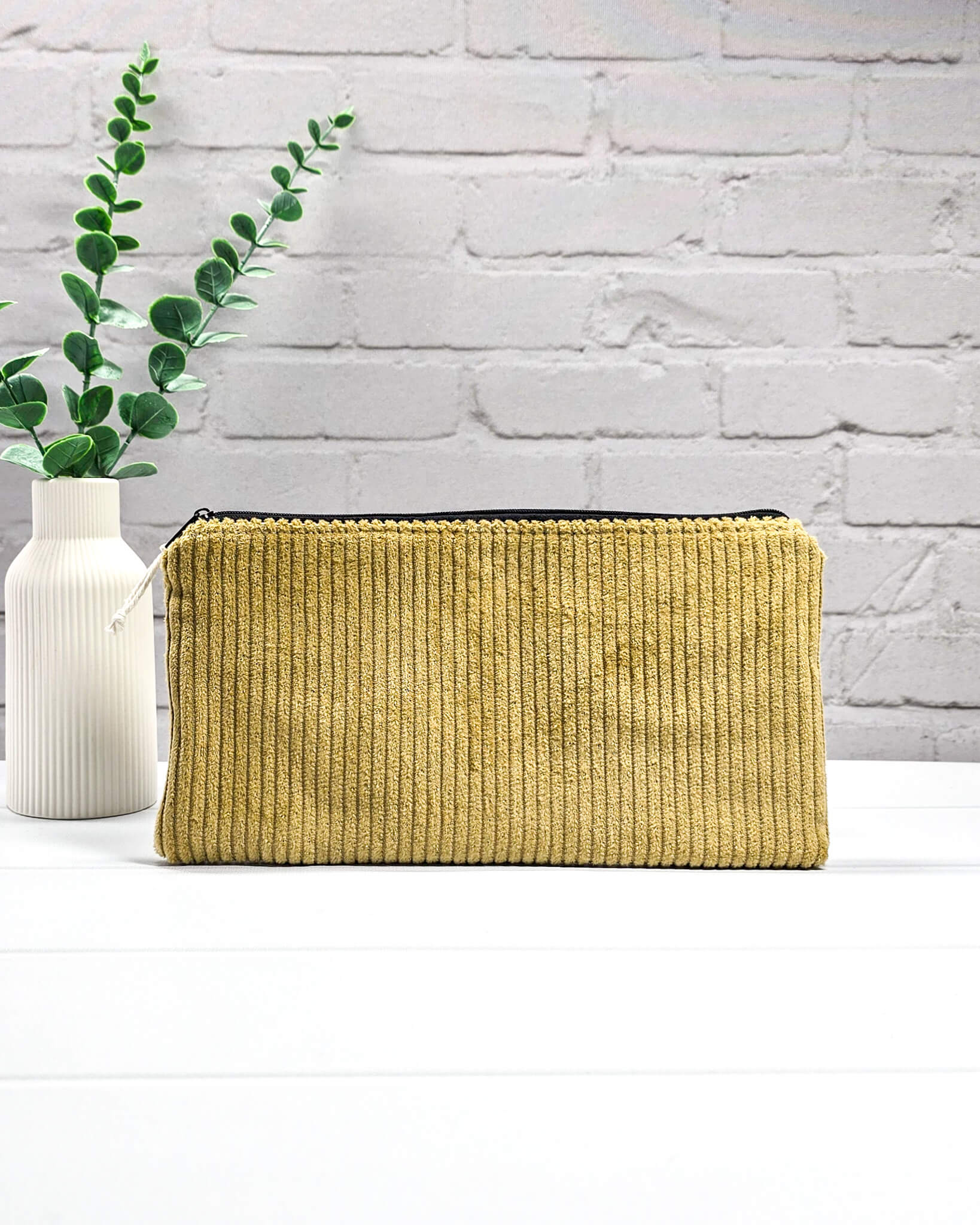 Kleine Reißverschlusstasche aus senfgelbem Cord-Stoff für Strickzubehör, flach liegend auf weißem Untergrund mit Schere, Garn und Nadeln. Handgenäht in Bayern von Nadelmikado.