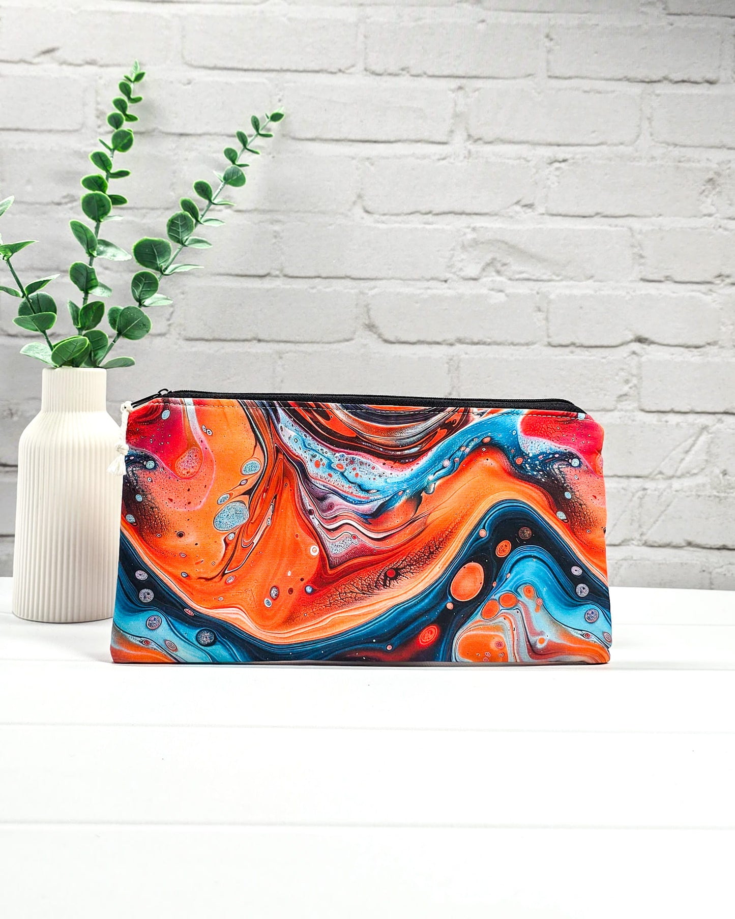 Längliches Täschchen mit schwarzem Reißverschluss, hellem Kordel-Zipper und buntem, fließendem Muster im Fluid-Art-Design mit Orange und Türkis. Handgenäht in Bayern von Nadelmikado.
