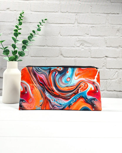 Längliches Täschchen mit schwarzem Reißverschluss, hellem Kordel-Zipper und buntem, fließendem Muster im Fluid-Art-Design mit Orange und Türkis. Handgenäht in Bayern von Nadelmikado.