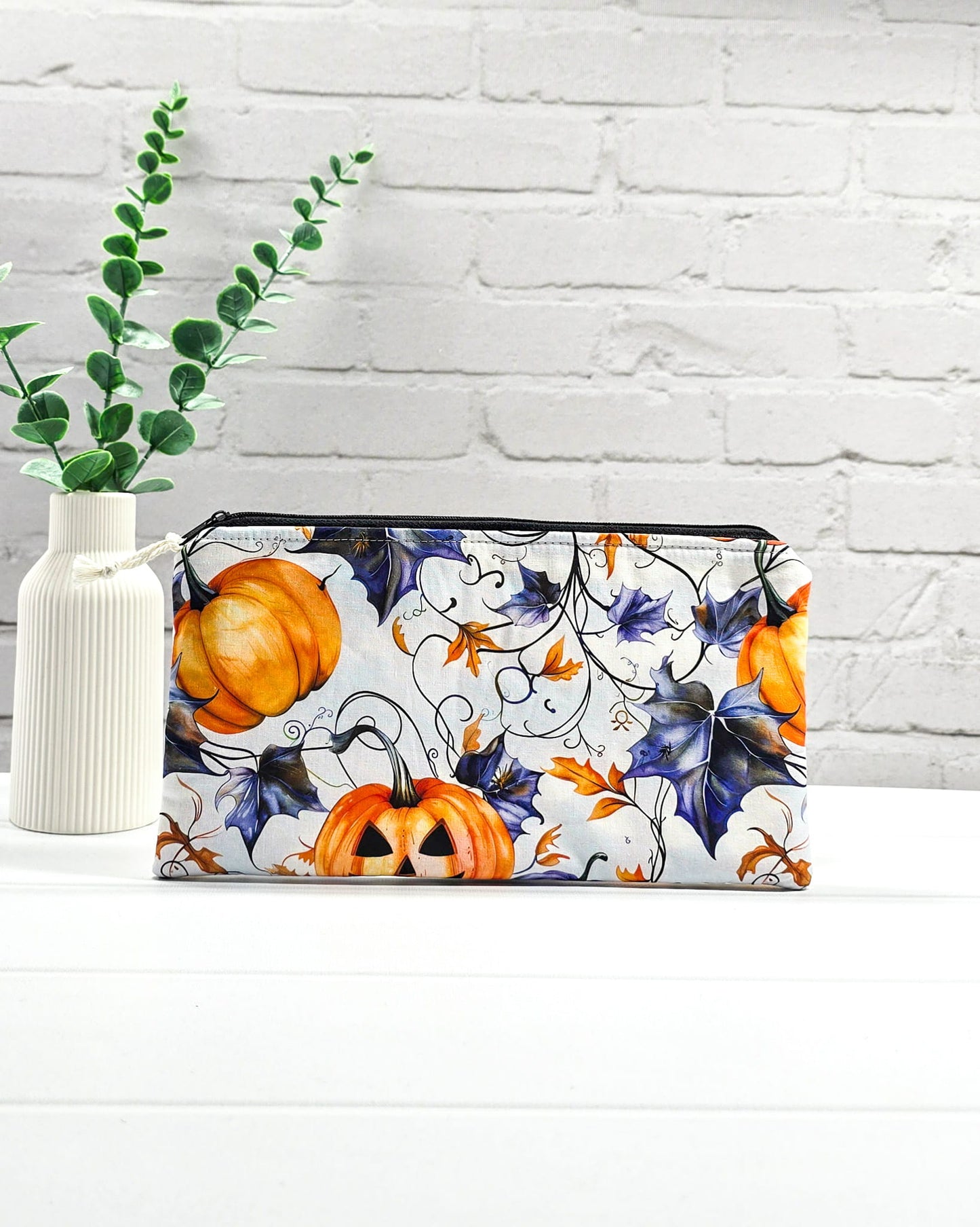 Handgenähte Zubehörtasche mit schwarzem Reißverschluss, weißem Kordel-Zipper und herbstlichen Halloween-Kürbissen auf hellem Stoff.