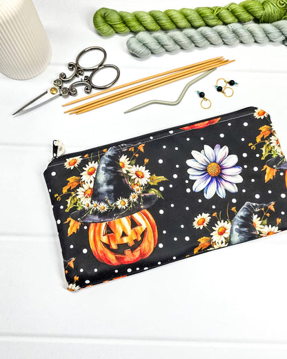 Längliche Zubehörtasche mit Reißverschluss und herbstlichen Kürbissen mit Hexenhüten, Blumen und Punkten auf schwarzem Grund. Handgenäht in Bayern von Nadelmikado.