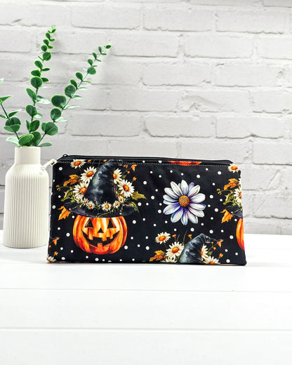 Längliche Zubehörtasche mit Reißverschluss und herbstlichen Kürbissen mit Hexenhüten, Blumen und Punkten auf schwarzem Grund. Handgenäht in Bayern von Nadelmikado.