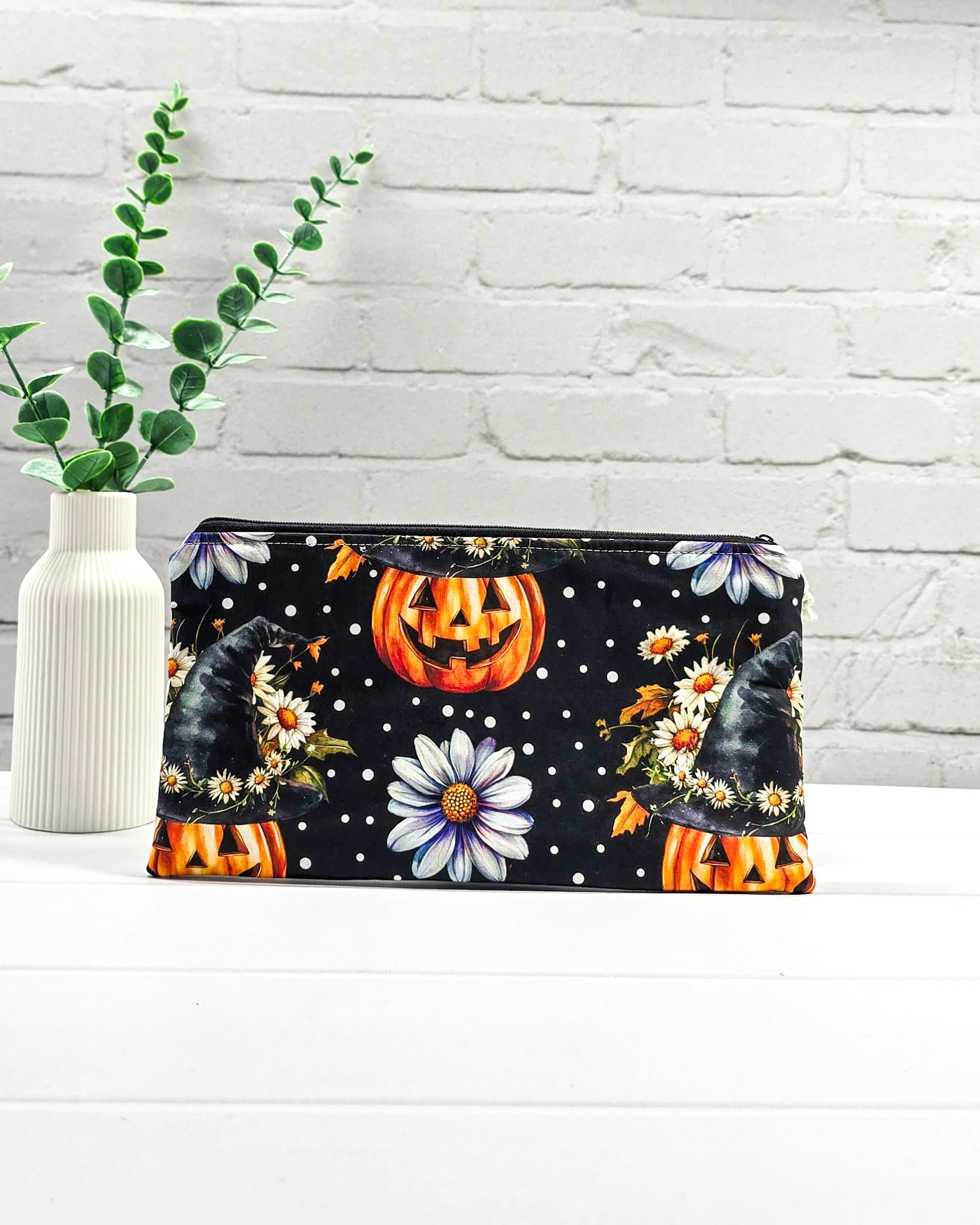 Längliche Zubehörtasche mit Reißverschluss und herbstlichen Kürbissen mit Hexenhüten, Blumen und Punkten auf schwarzem Grund. Handgenäht in Bayern von Nadelmikado.