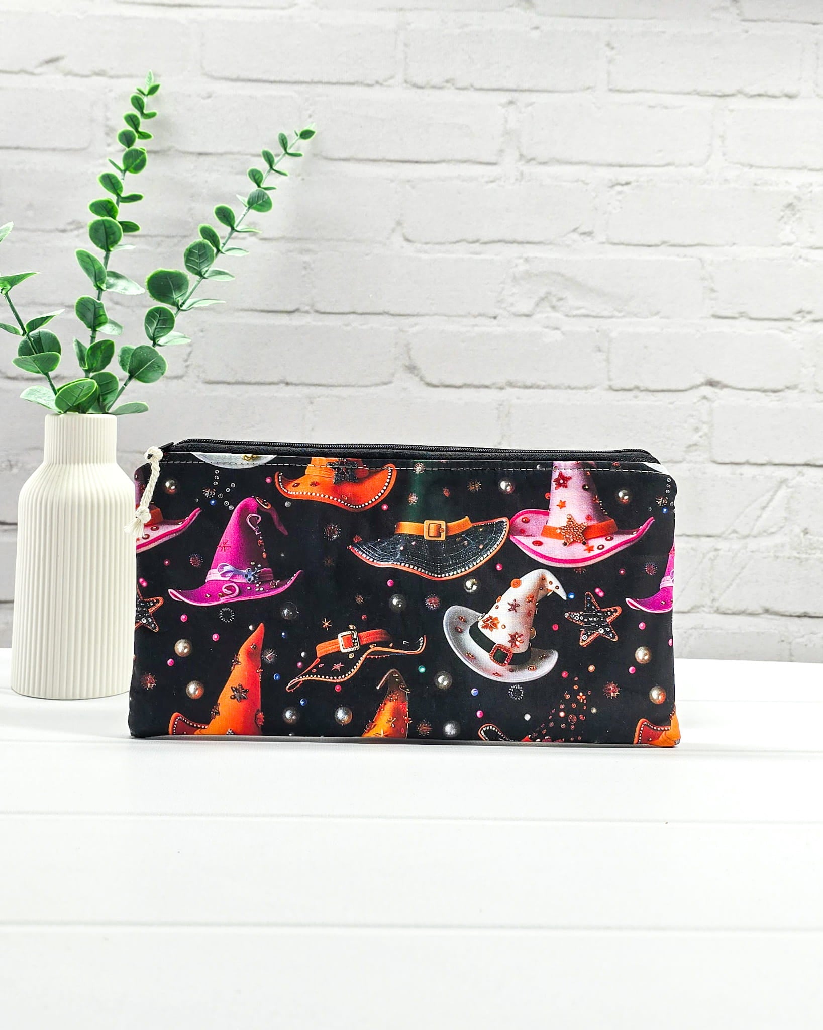 Kleine Reißverschlusstasche aus schwarzem Stoff mit bunten Hexenhüten als Zubehör-Etui für Handarbeiten. Genäht in Bayern von Nadelmikado.
