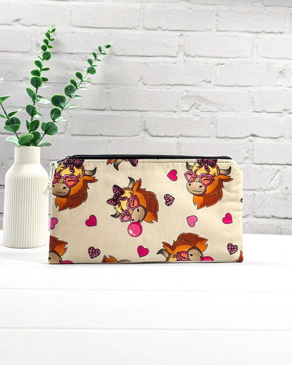 Längliche Tasche mit schwarzem Reißverschluss, hellem Kordel-Zipper und lustigem Highland-Cattle-Motiv mit Herzbrillen auf beigem Stoff. Handgenäht in Bayern von Nadelmikado.