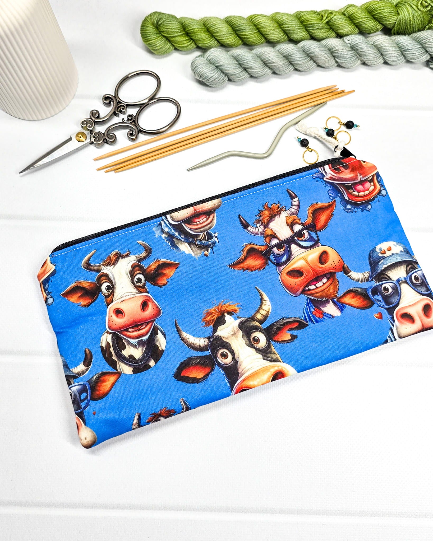 Flaches Reißverschlusstäschchen mit witzigen Kuh-Motiven auf blauem Stoff und hellem Kordel-Zipper. Handgenäht in Bayern von Nadelmikado.