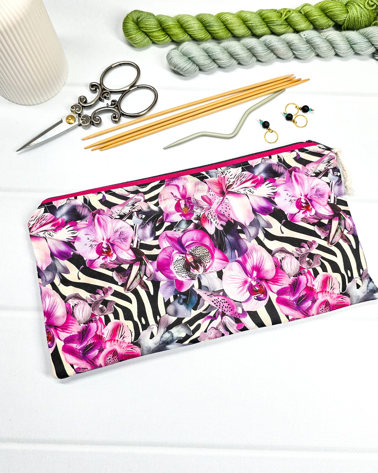 Längliche Tasche mit pinkfarbenem Reißverschluss, hellem Kordel-Zipper und auffälligem Muster aus lila Orchideenblüten über einem schwarz-weißen Zebramuster. Handgenäht in Bayern von Nadelmikado.