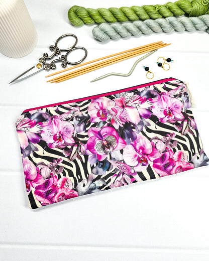 Längliche Tasche mit pinkfarbenem Reißverschluss, hellem Kordel-Zipper und auffälligem Muster aus lila Orchideenblüten über einem schwarz-weißen Zebramuster. Handgenäht in Bayern von Nadelmikado.