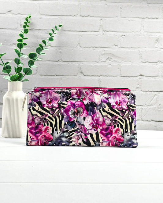 Längliche Tasche mit pinkfarbenem Reißverschluss, hellem Kordel-Zipper und auffälligem Muster aus lila Orchideenblüten über einem schwarz-weißen Zebramuster. Handgenäht in Bayern von Nadelmikado.