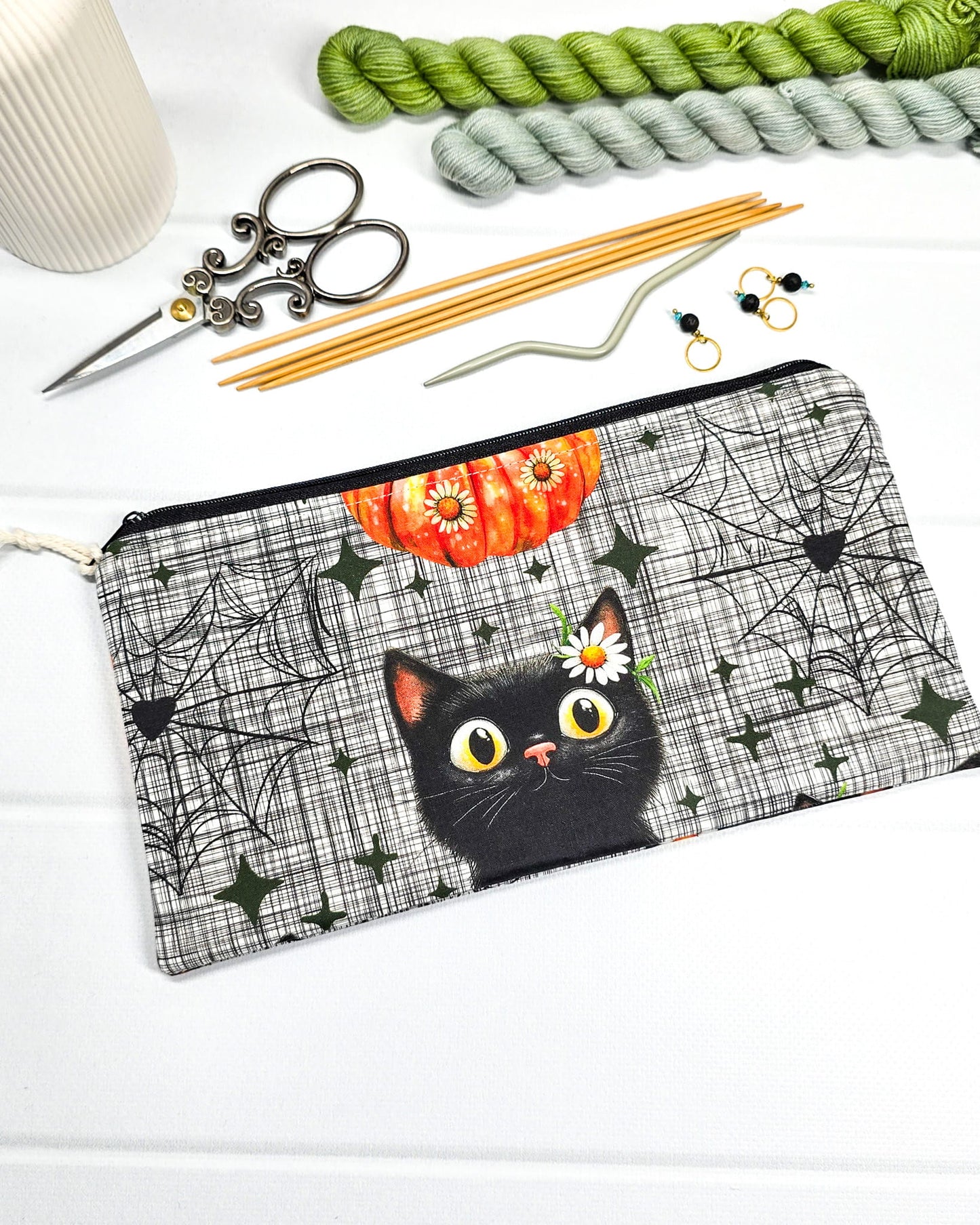 Längliche Zubehörtasche mit schwarzem Reißverschluss, hellem Kordel-Zipper und einer schwarzen Katze vor Spinnweben. Handgenäht in Bayern von Nadelmikado.
