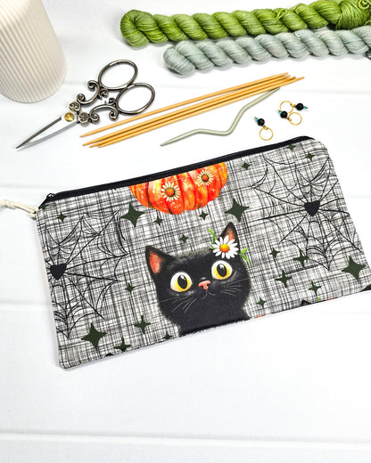Längliche Zubehörtasche mit schwarzem Reißverschluss, hellem Kordel-Zipper und einer schwarzen Katze vor Spinnweben. Handgenäht in Bayern von Nadelmikado.
