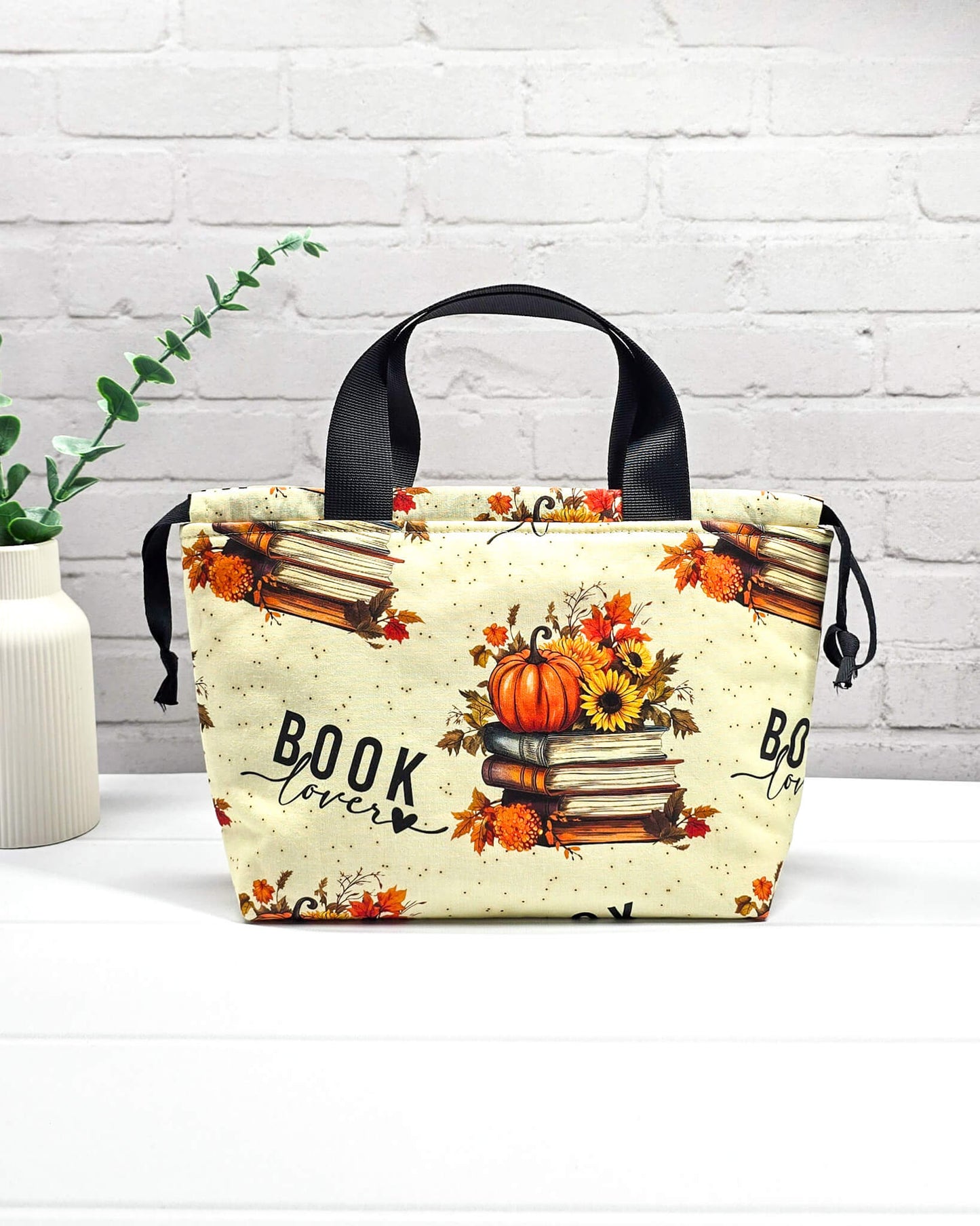 Projekttasche Alva S mit herbstlichem „Book Lover“-Motiv, Bücherstapeln und Kürbissen auf cremefarbenem Stoff. Handgenäht in Bayern von Nadelmikado
