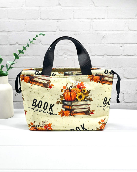 Projekttasche Alva S mit herbstlichem „Book Lover“-Motiv, Bücherstapeln und Kürbissen auf cremefarbenem Stoff. Handgenäht in Bayern von Nadelmikado