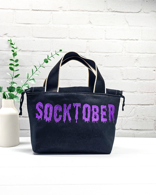 Schwarze Stricktasche Alva S mit violettem Socktober-Schriftzug, handgenäht und bestickt in Bayern von NadelMikado