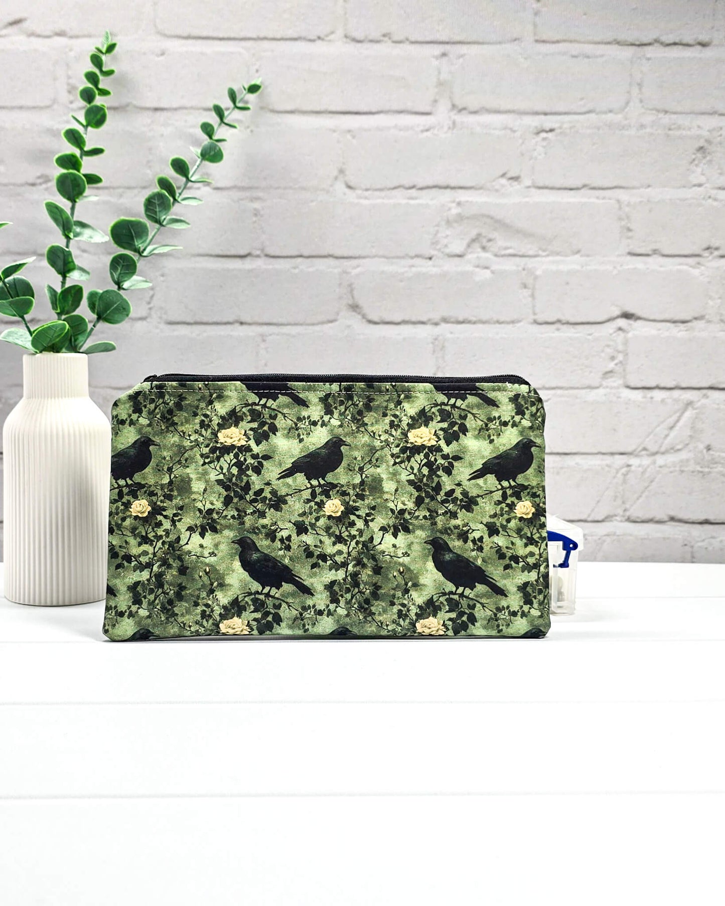 Grüne Tasche mit Reißverschluss, gemustert mit Raben und Rosen, genutzt für Handarbeitszubehör. Handgenäht in Bayern von Nadelmikado.