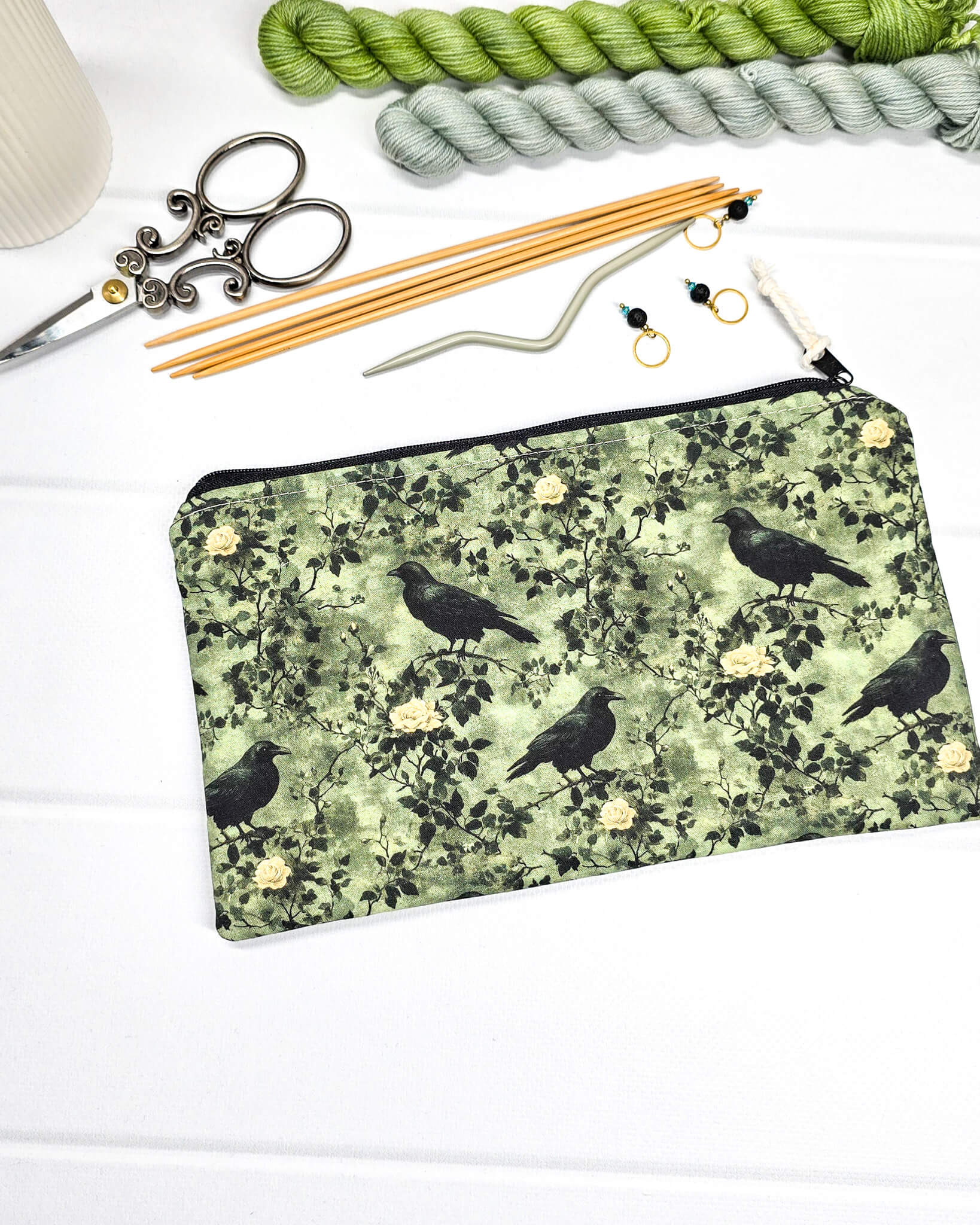 Grüne Tasche mit Reißverschluss, gemustert mit Raben und Rosen, genutzt für Handarbeitszubehör. Handgenäht in Bayern von Nadelmikado.