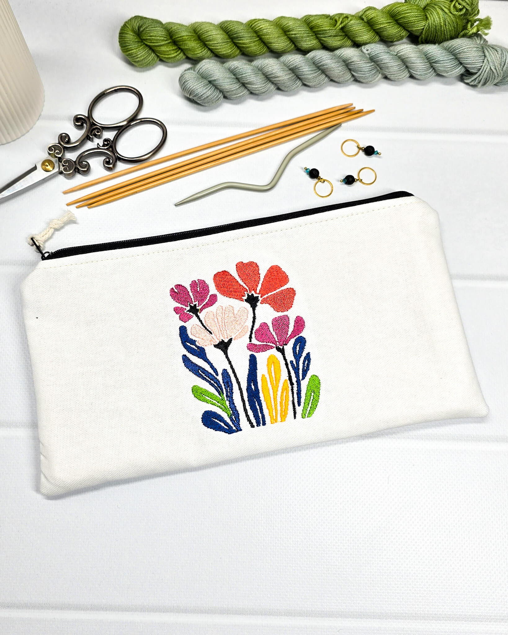 Flaches, weißes Canvas-Etui Runa mit bunter Wildblumen-Stickerei, entworfen zur sicheren und knickfreien Aufbewahrung von Stricknadeln, Nadelseilen und Scheren im Projektbeutel. Handgenäht in Bayern von Nadelmikado.