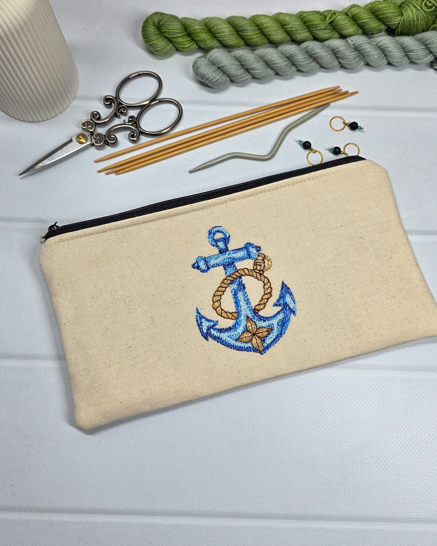 Flache, rechteckige Zip Pouch Runa aus beigem Canvas mit einem großen, blau-gold gestickten Schiffsanker, ideal um Stricknadeln, Seile und Scheren sicher zu verwahren. Handgenäht in Bayern von Nadelmikado