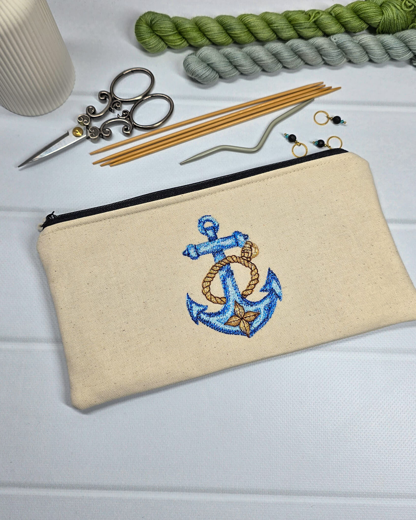 Flache, rechteckige Zip Pouch Runa aus beigem Canvas mit einem großen, blau-gold gestickten Schiffsanker, ideal um Stricknadeln, Seile und Scheren sicher zu verwahren. Handgenäht in Bayern von Nadelmikado