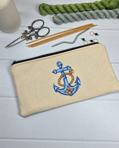 Flache, rechteckige Zip Pouch Runa aus beigem Canvas mit einem großen, blau-gold gestickten Schiffsanker, ideal um Stricknadeln, Seile und Scheren sicher zu verwahren. Handgenäht in Bayern von Nadelmikado