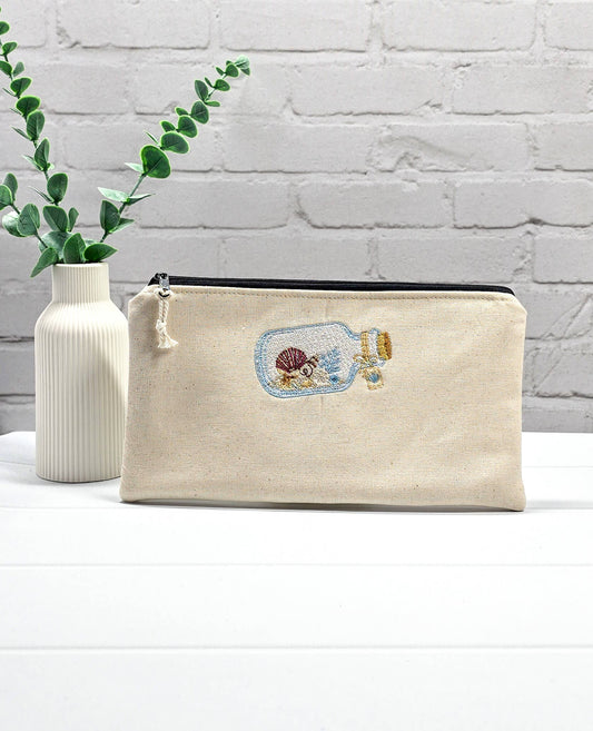 Flache, rechteckige Zip Pouch Runa aus beigem Canvas mit einer gestickten Glasflasche voller kleiner Muscheln, handgenäht in Bayern von Nadelmikado