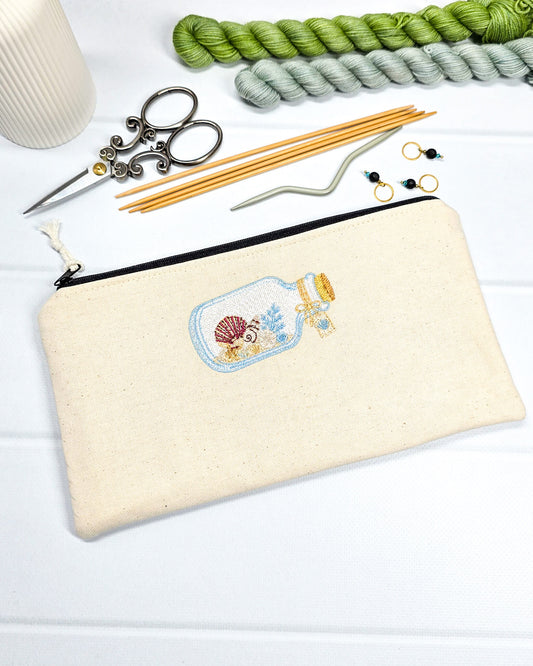 Flache, rechteckige Zip Pouch Runa aus beigem Canvas mit einer gestickten Glasflasche voller kleiner Muscheln, handgenäht in Bayern von Nadelmikado