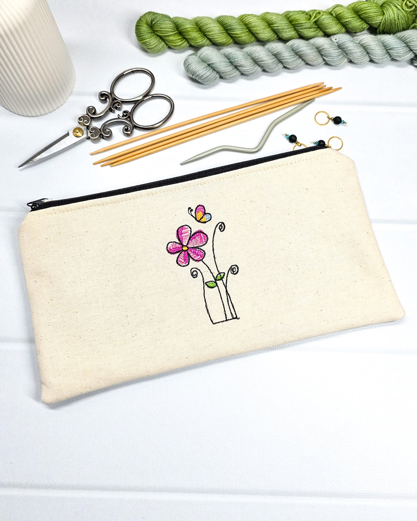 Flache, rechteckige Zip Pouch Runa aus beigem Canvas mit einer zierlich gestickten Blume und einem Schmetterling, perfekt zum geschützten Aufbewahren von Stricknadeln und Zubehör. Handgenäht in Bayern von Nadelmikado.