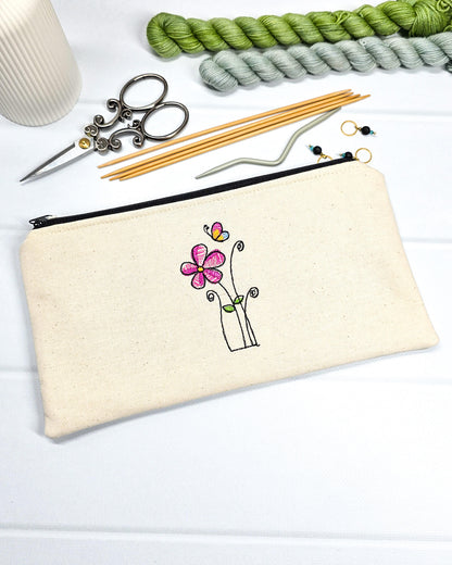Flache, rechteckige Zip Pouch Runa aus beigem Canvas mit einer zierlich gestickten Blume und einem Schmetterling, perfekt zum geschützten Aufbewahren von Stricknadeln und Zubehör. Handgenäht in Bayern von Nadelmikado.