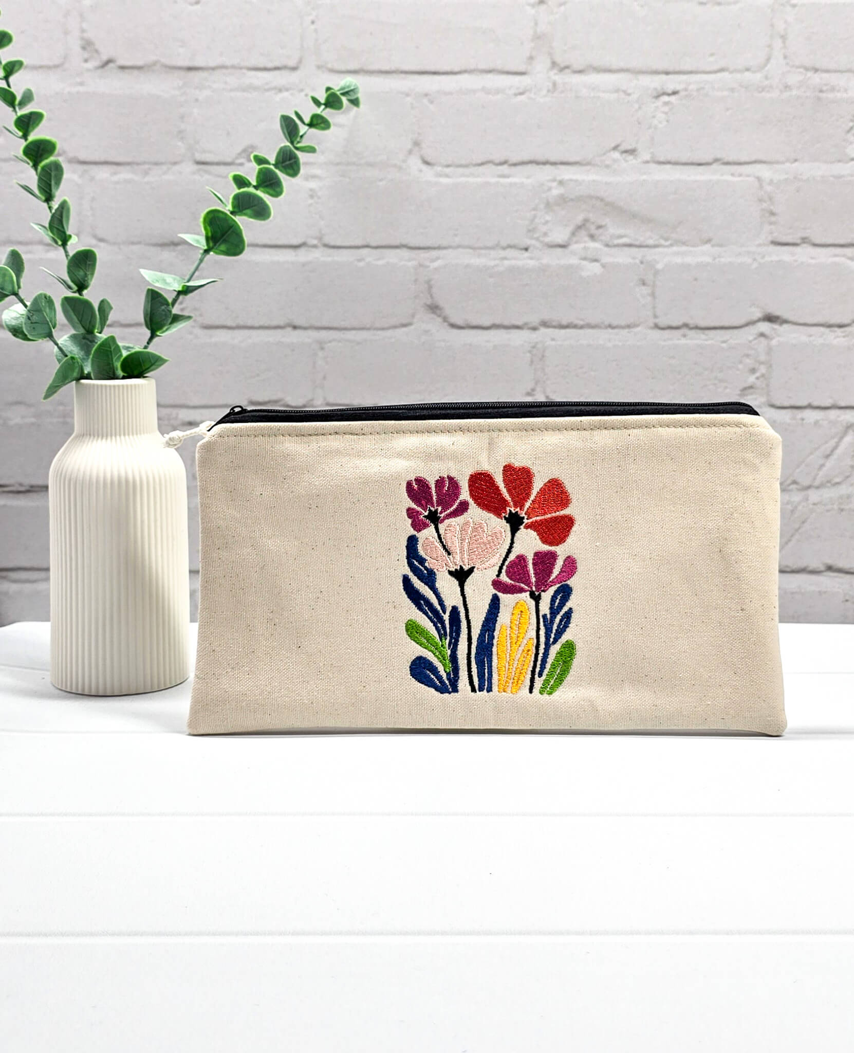 Flache, rechteckige Zip Pouch Runa aus beigem Canvas mit einer großen, bunt gestickten Blumengruppe, ideal zum platzsparenden Einsortieren von Stricknadeln und Seilen. Handgenäht in Bayern von Nadelmikado.