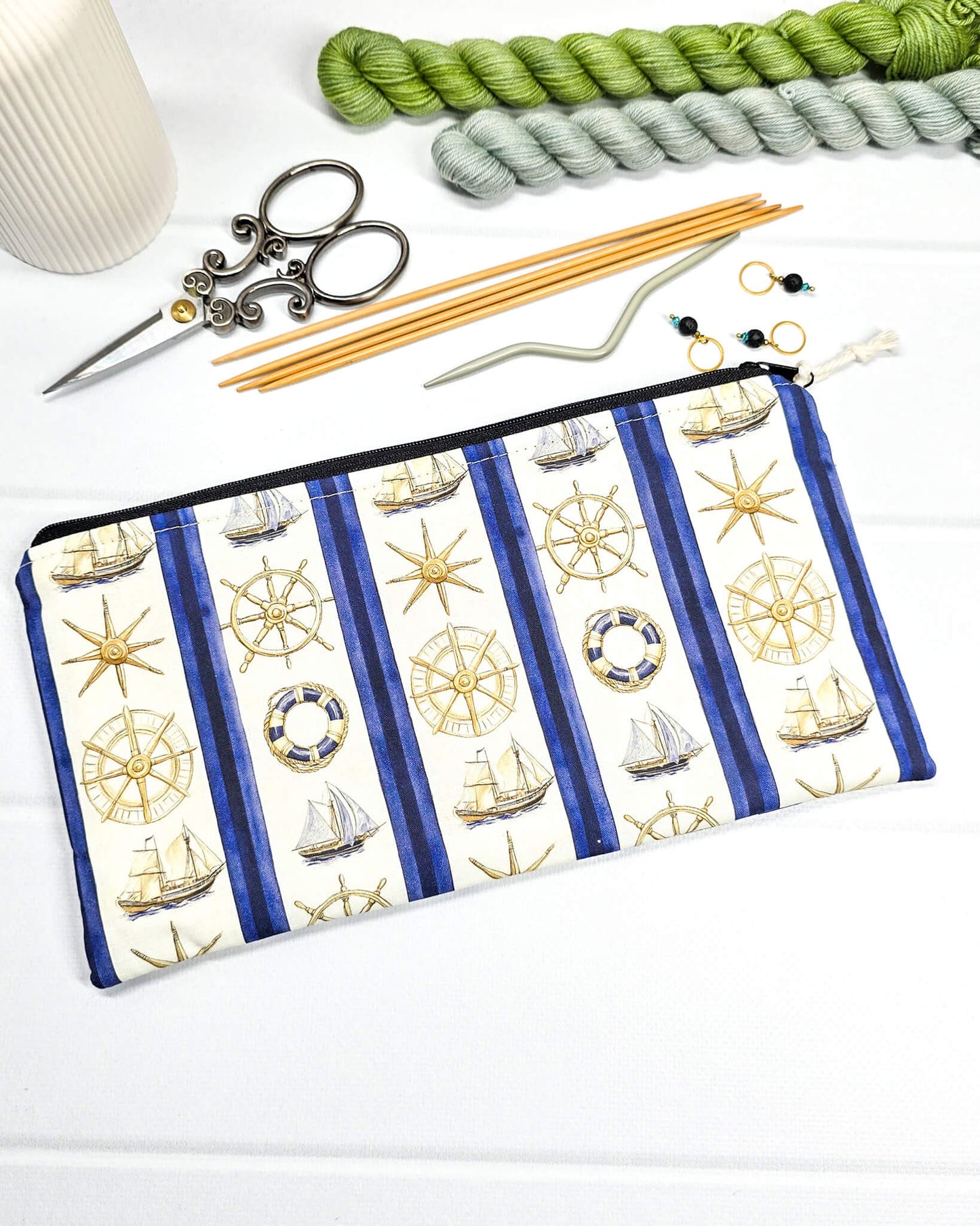 Flache, rechteckige Zip Pouch Runa mit maritimen Motiven wie Segelschiffen und Steuerrädern zwischen blau-weißen Streifen, handgenäht in Bayern von Nadelmikado. 