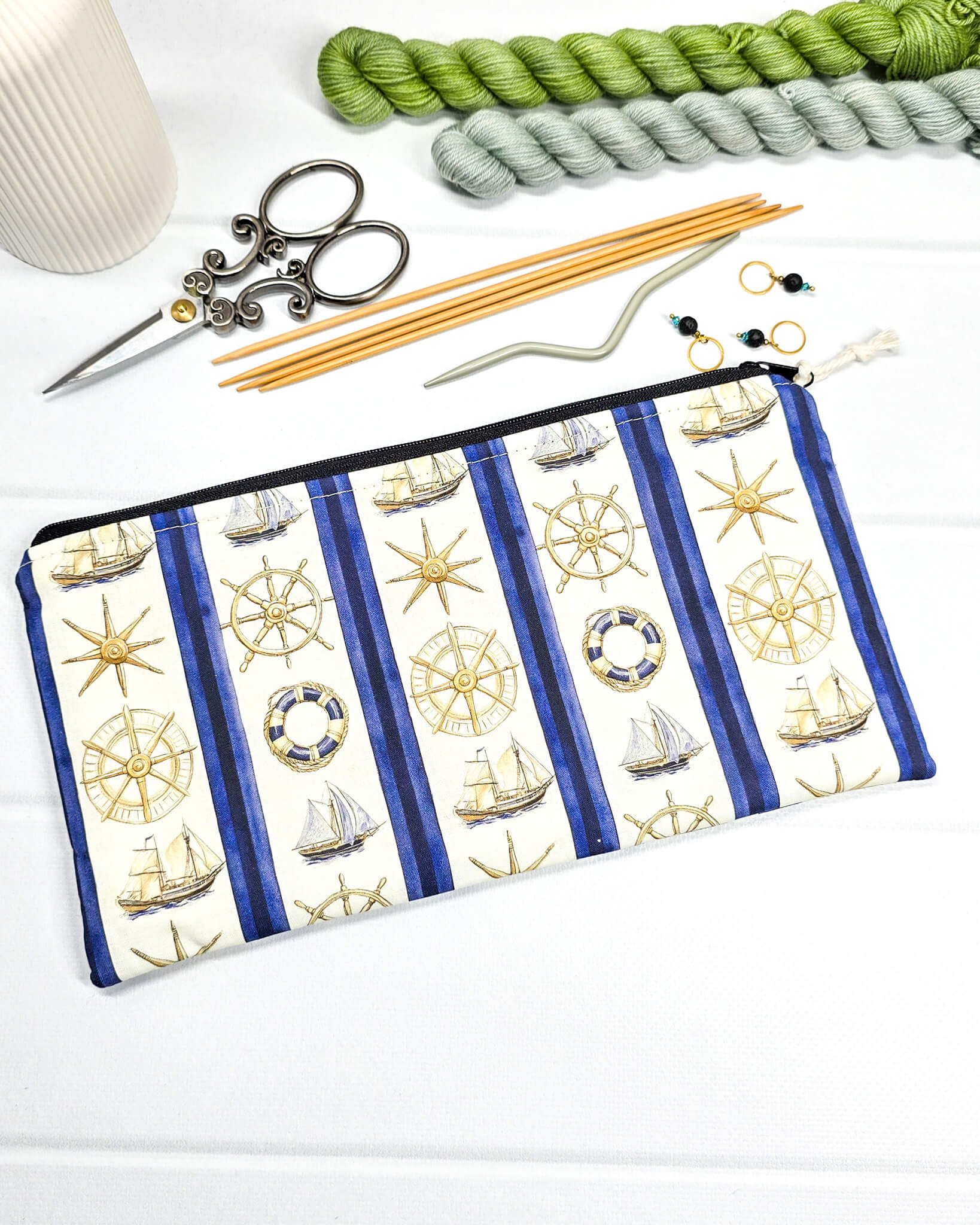Flache, rechteckige Zip Pouch Runa mit maritimen Motiven wie Segelschiffen und Steuerrädern zwischen blau-weißen Streifen, handgenäht in Bayern von Nadelmikado. 